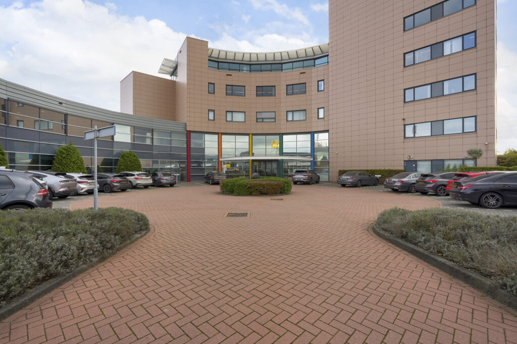 Een modern kantoorpand aan de Laan van ’s-Gravenmade met een halve rotonde en geparkeerde auto's op de voorgrond.