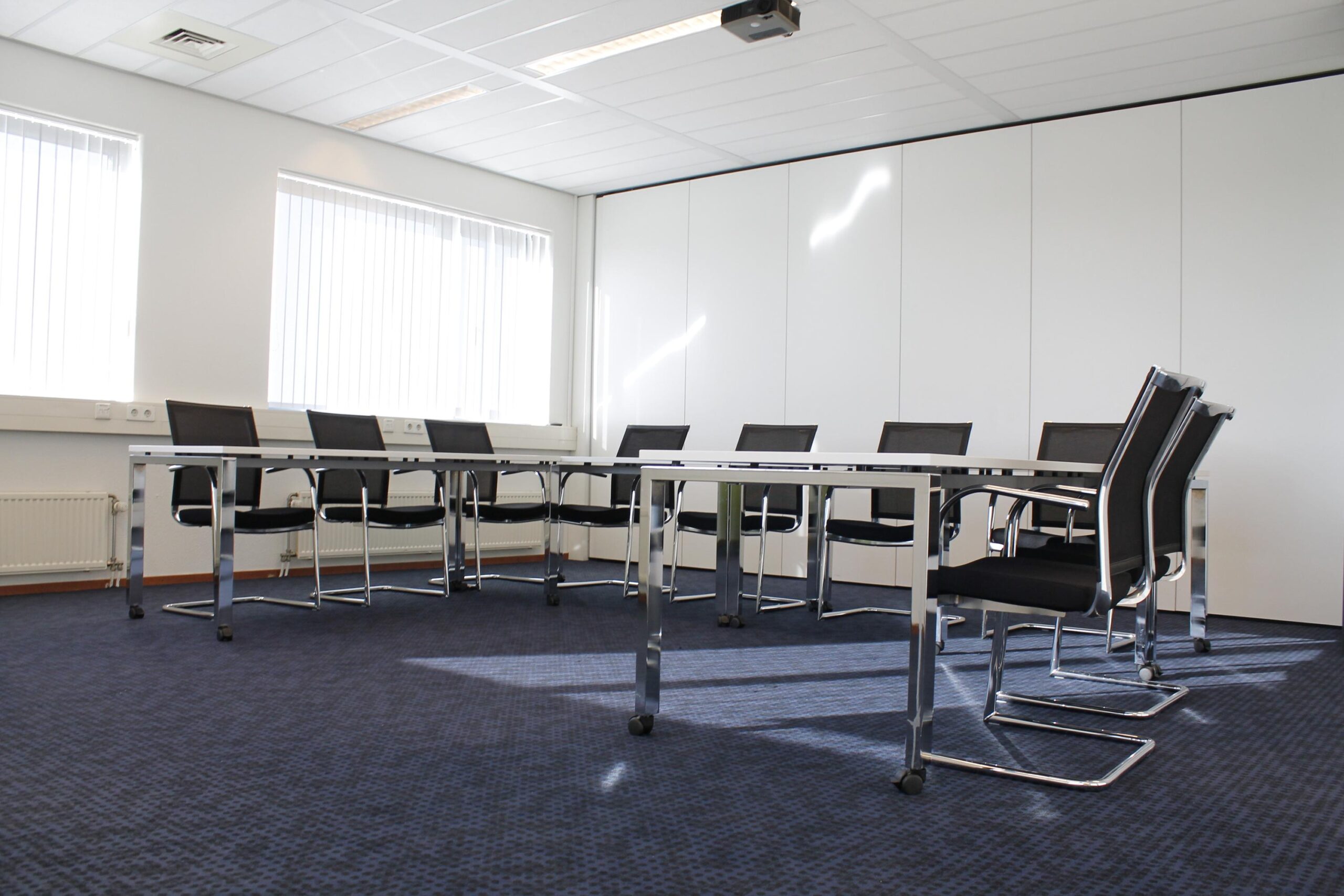 Vergaderruimte aan de Laan van ’s-Gravenmade met moderne stoelen, tafels en witte wandpanelen.