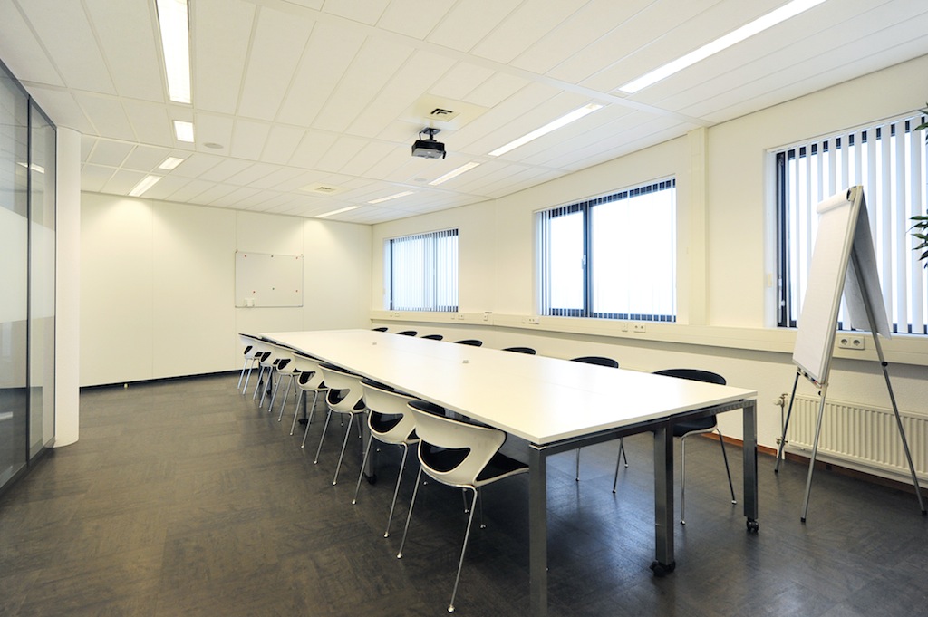 Vergaderruimte aan de Laan van S'Gravenmade met lange tafel, stoelen, whiteboard en flip-over in een lichte, moderne inrichting.