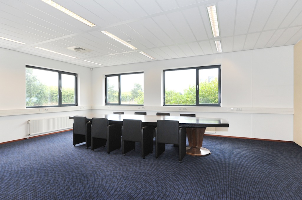 Vergaderruimte aan de Laan van S-Gravenmade met grote tafel, acht zwarte stoelen en veel daglicht door drie ramen.