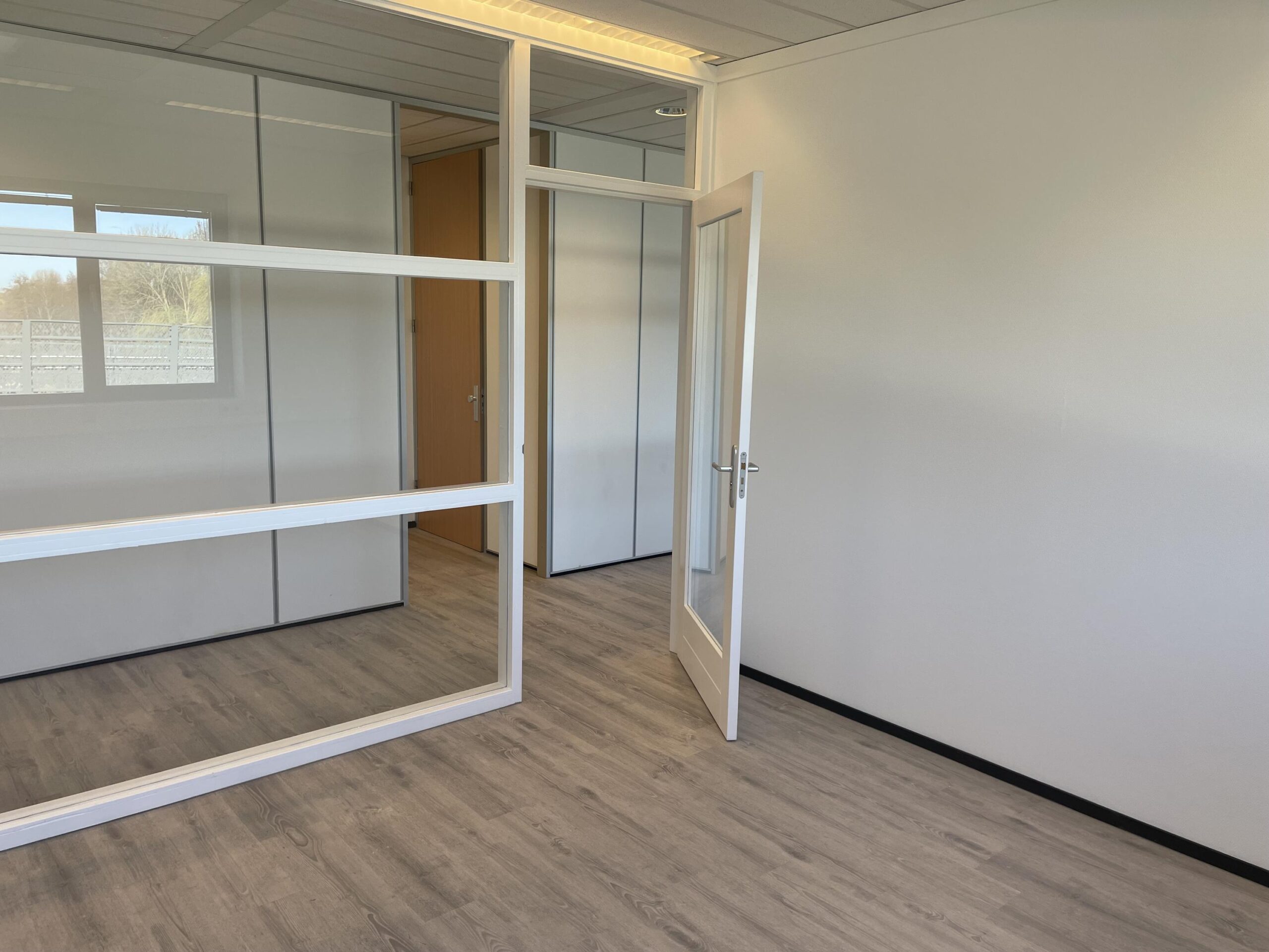Leeg en modern kantoor met glazen binnenwanden en een open deur aan de Laan van ‘s-Gravenmade.