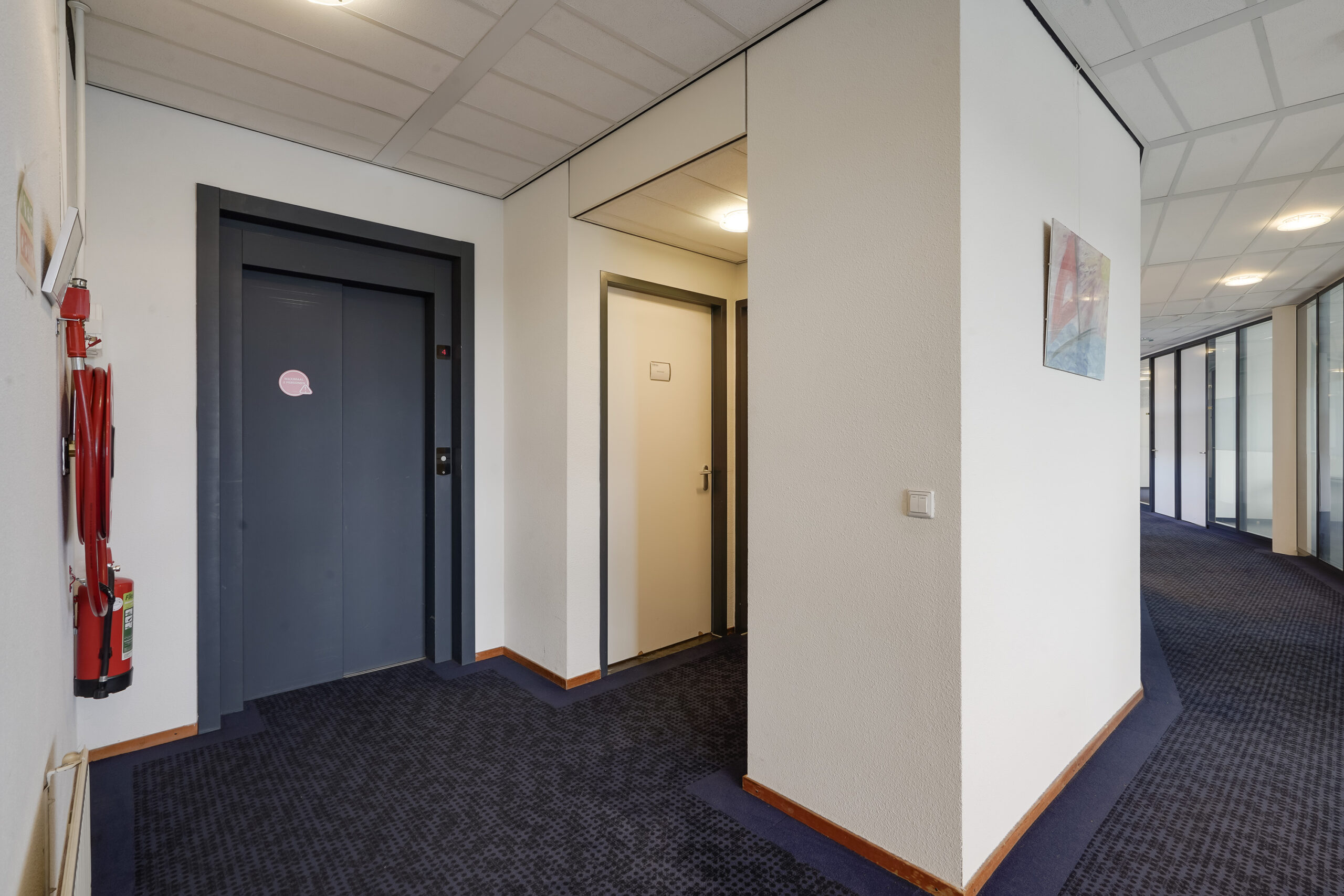 Binnenhal met een lift, een deur en een gang in een kantoorpand aan de Laan van ’s-Gravenmade.