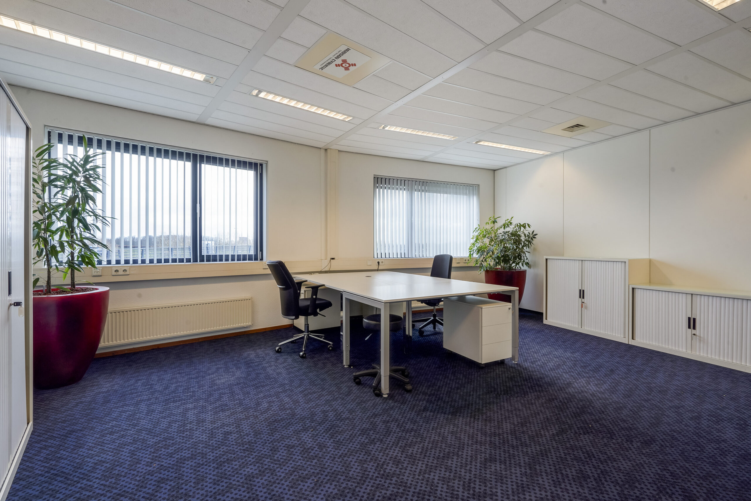 Modern ingericht kantoor aan de Laan van S‑Gravenmade met twee bureaustoelen, grote ramen en planten in rode potten.