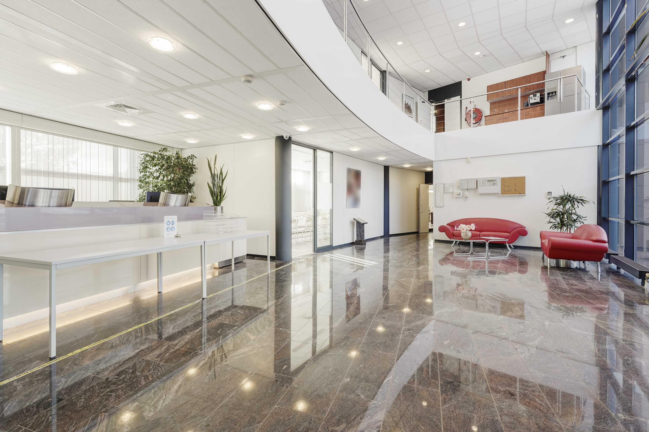 Moderne en lichte ontvangsthal aan de Laan van ’s-Gravenmade met glanzende marmeren vloer, balie en rode zithoek.