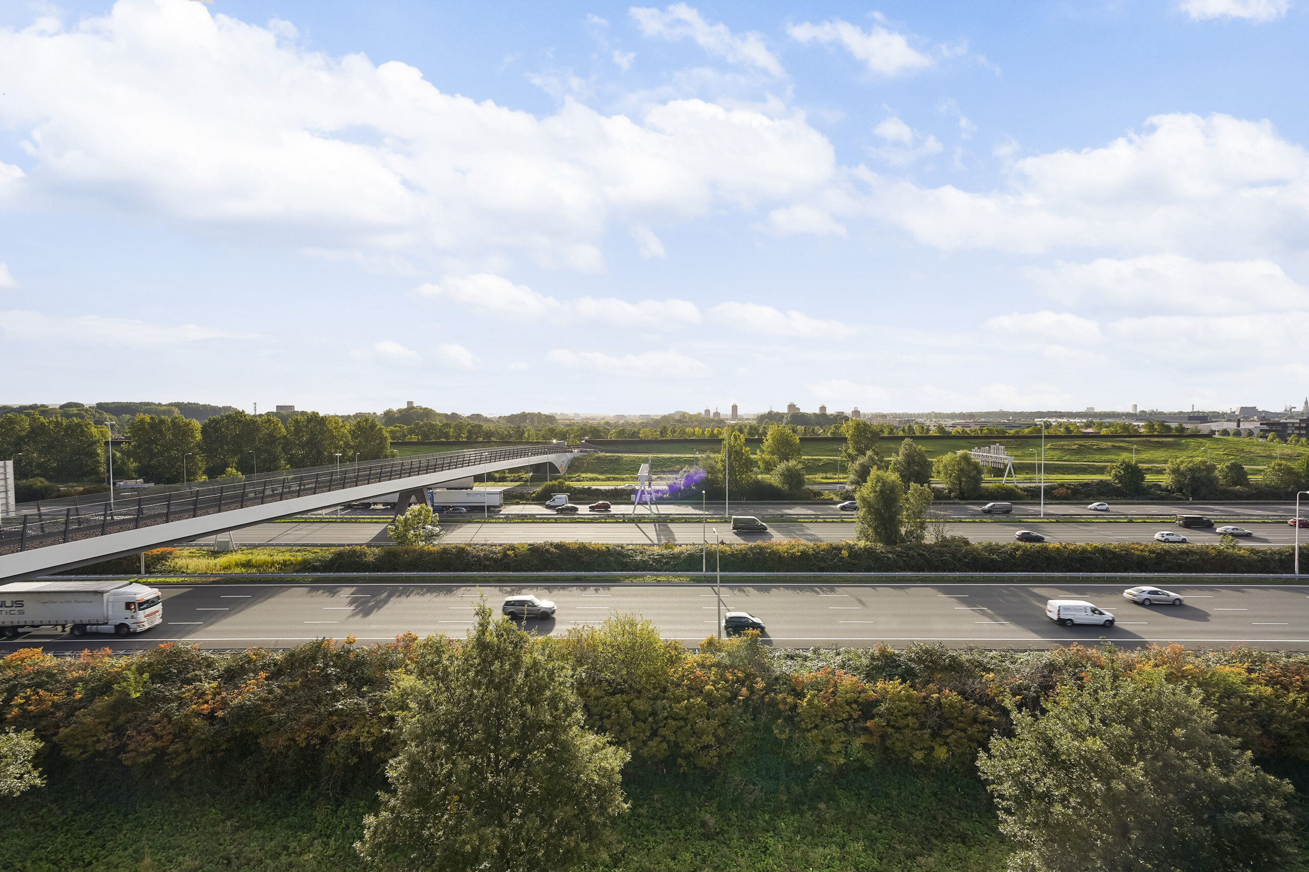 Wegzicht op de Laan van S-Gravenmade met een fietsbrug over de snelweg en groen landschap op de achtergrond.