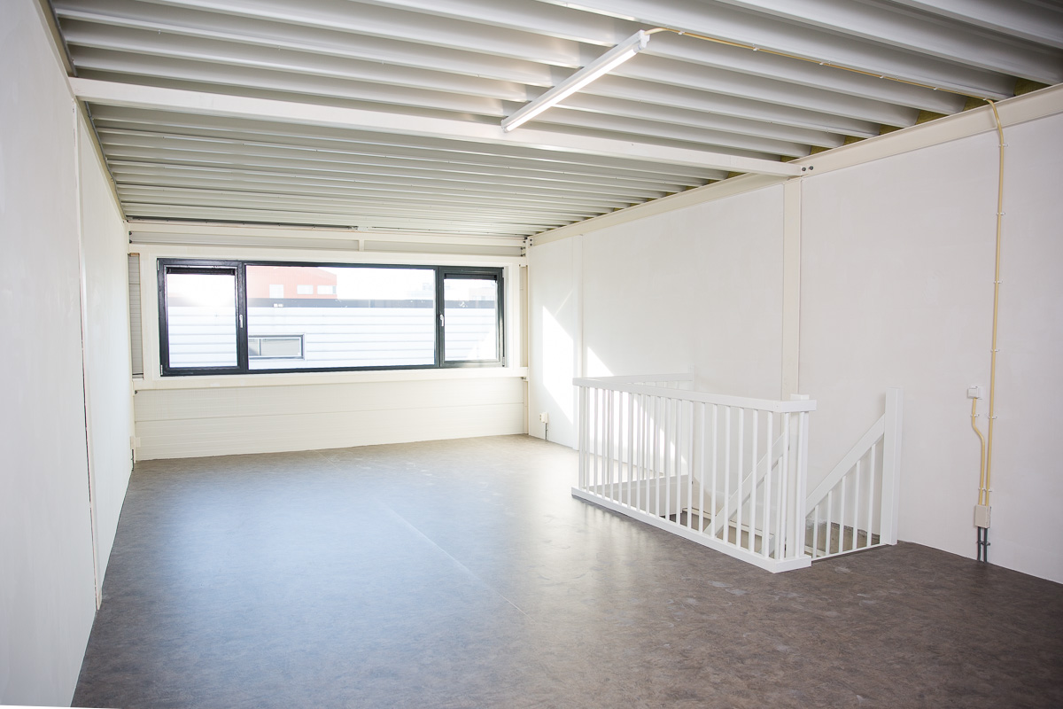 Leeg kantoor- of bedrijfsruimte op de eerste verdieping aan de Laan van ’s-Gravenmade met grote ramen en een witte trapleuning.