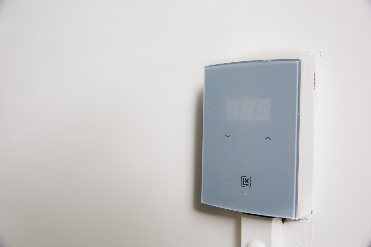 Close-up van een grijze LK-thermostaat aan de muur met een scherm dat 19,5 graden Celsius weergeeft.