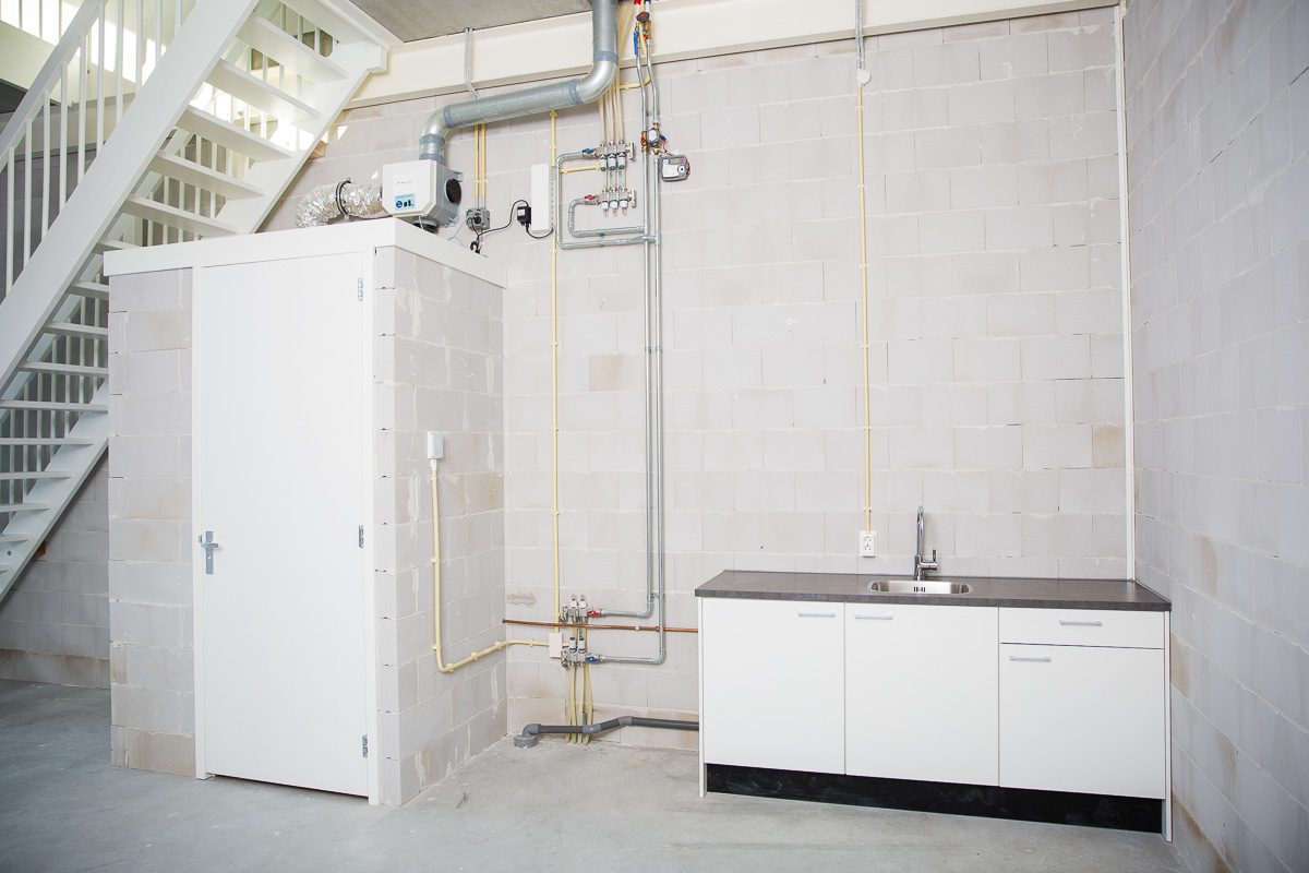 Witte pantry met gootsteen en technische installaties tegen een betonnen muur in een bedrijfsruimte aan de Laan van s-Gravenmade.