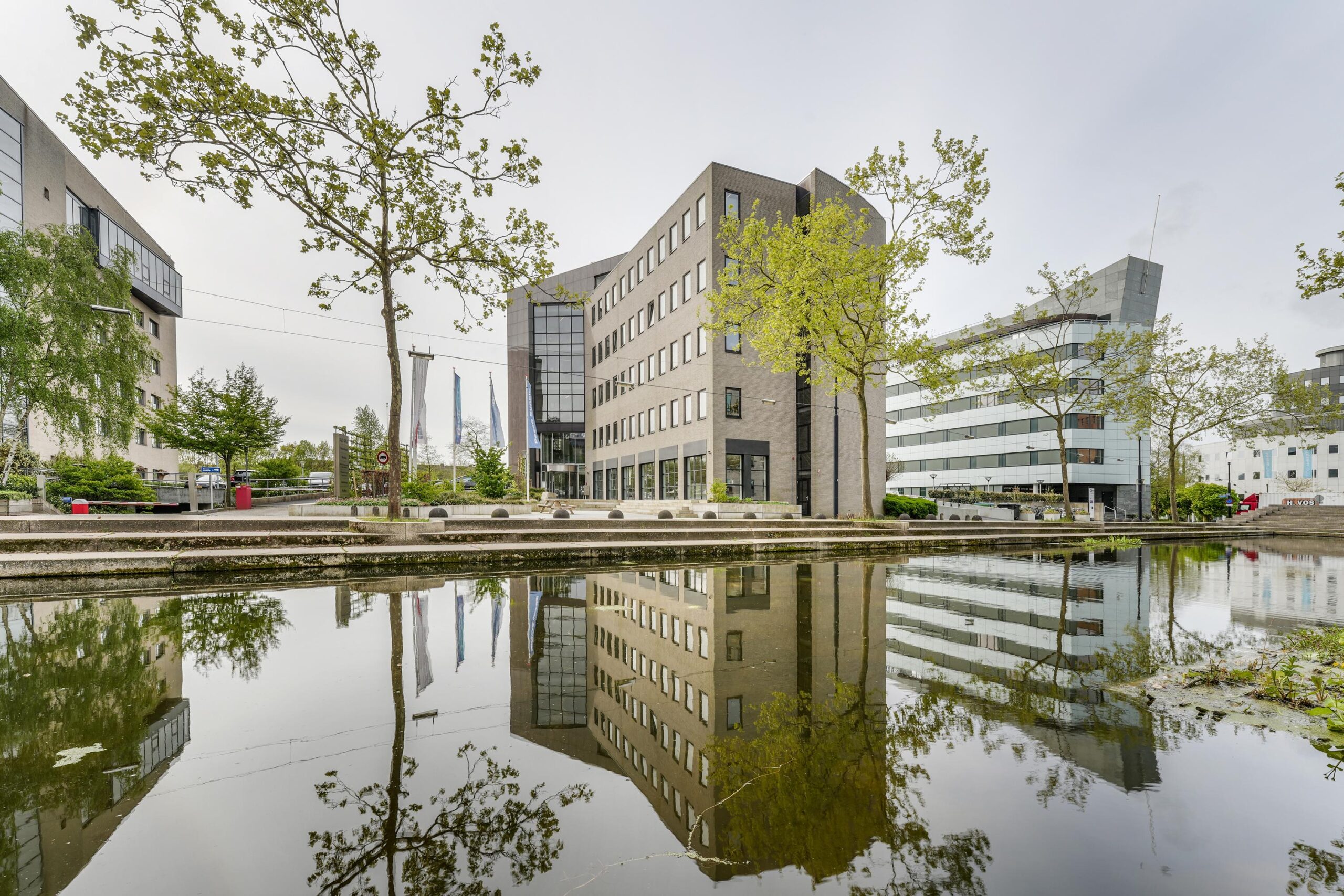 Modern kantoorgebouw aan de Euclideslaan in Utrecht, weerspiegeld in een vijver met omliggende bomen.