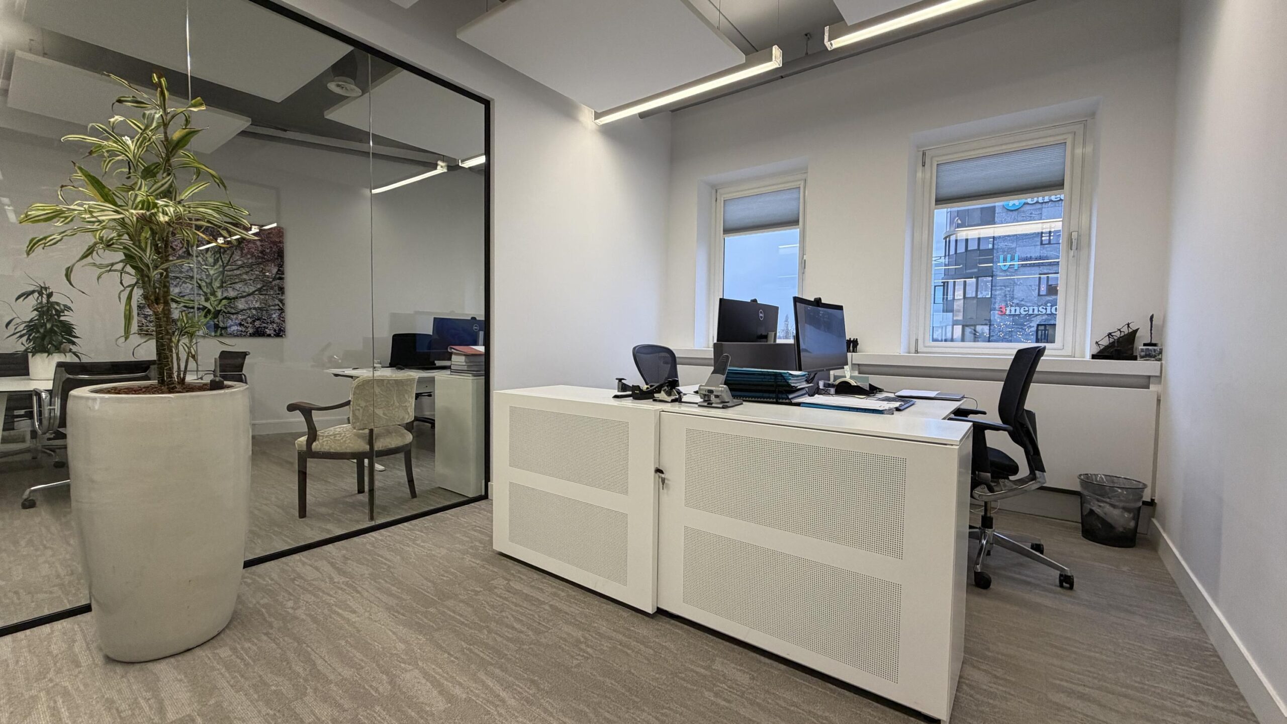 Modern kantoorinterieur aan de Euclideslaan met bureaus, computers, kamerplanten en uitzicht op een tegenoverliggend gebouw.