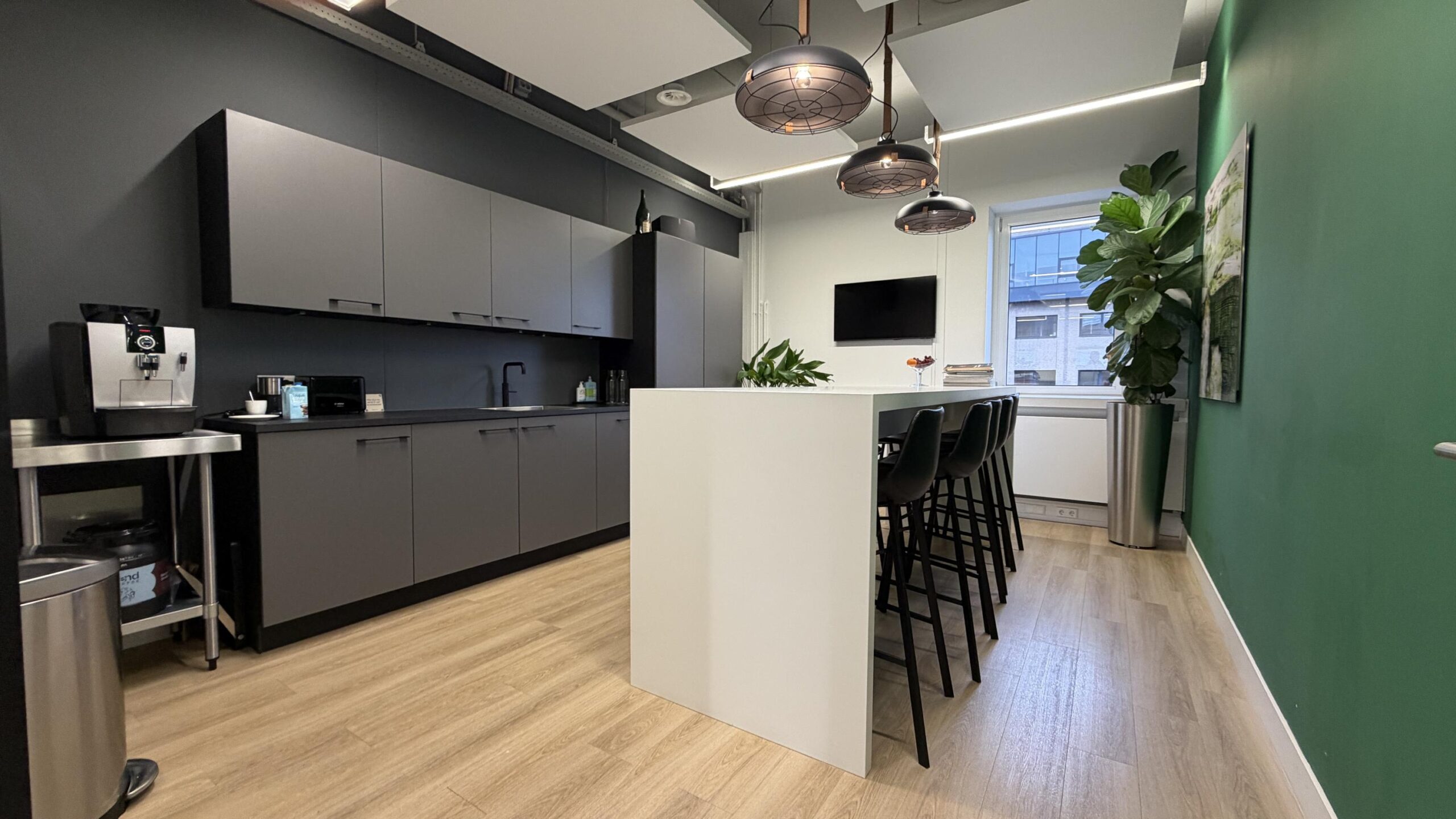 Moderne kantoorkeuken aan de Euclideslaan met strakke grijze kasten, een koffiezetapparaat en een hoge witte eettafel met barkrukken.