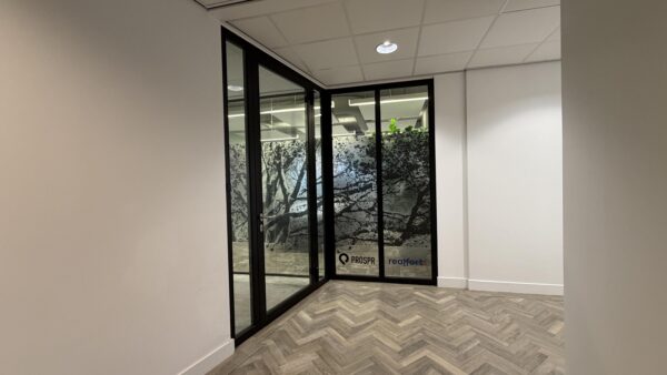 Ingang van een modern kantoor aan de Euclideslaan met glazen wanden en decoratieve boomprint, met logo’s van PROSPR en realfort.