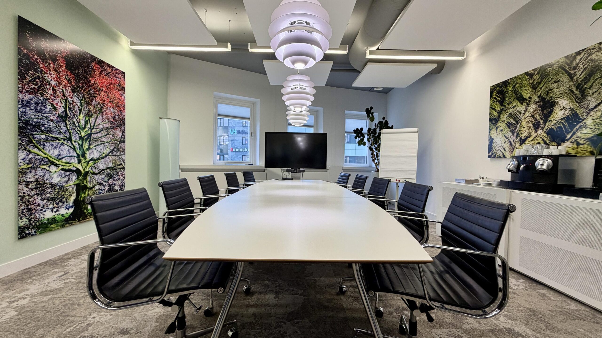 Moderne vergaderruimte aan de Euclideslaan met een lange tafel, leren stoelen, een scherm, koffiezetapparaat en grote muurkunst.