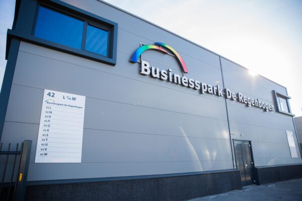 Vooraanzicht van een modern bedrijfsgebouw met het logo en de naam "Businesspark De Regenbogen" aan de Laan van S-Gravenmade.