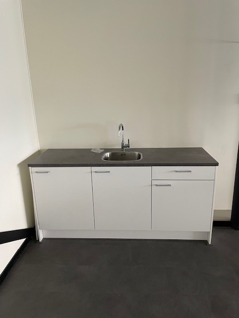 Witte kitchenette met donker aanrechtblad en spoelbak in een lege ruimte aan de Laan van S’Gravenmade.
