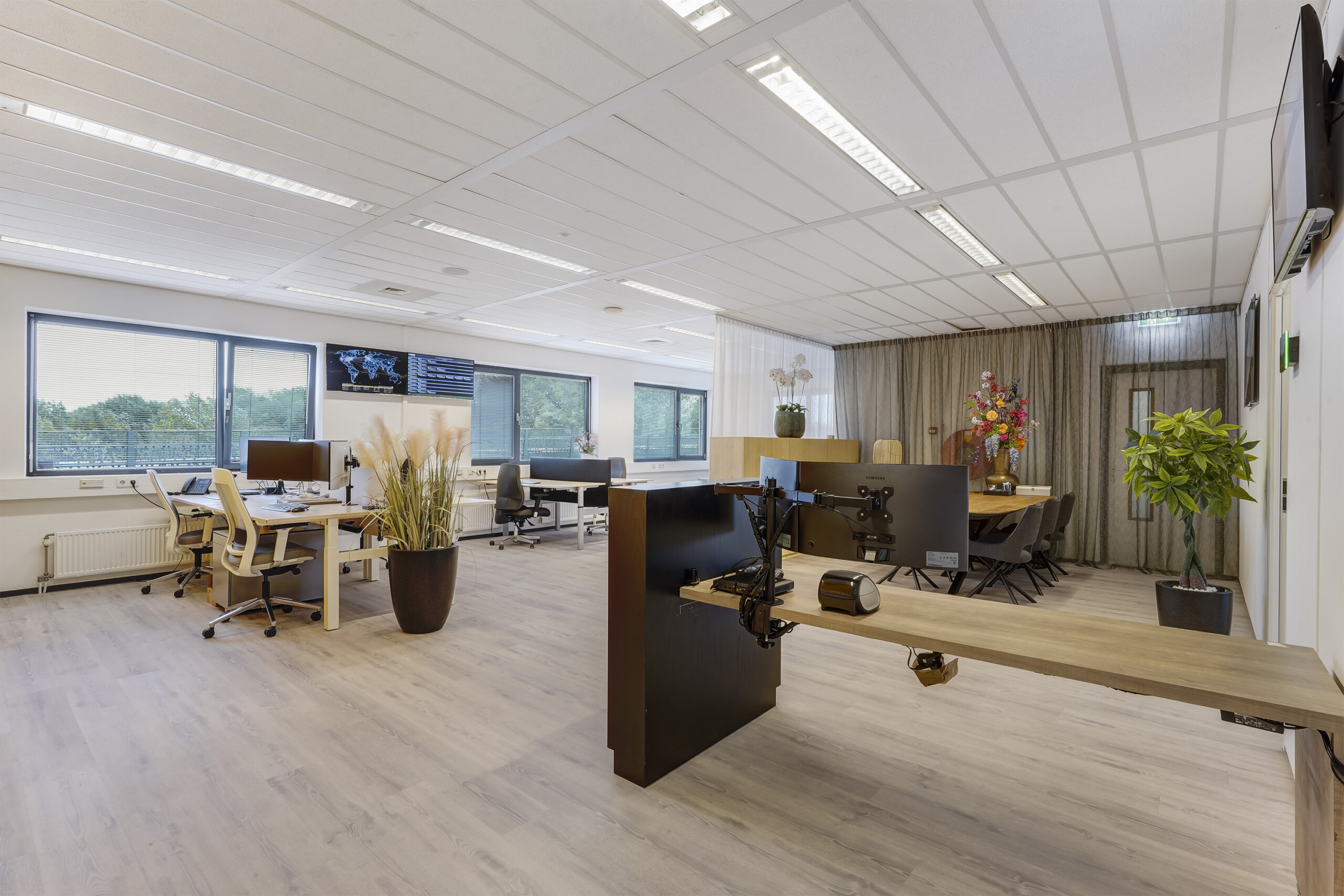 Modern en licht kantoorinterieur aan de Laan van 's-Gravenmade met bureaus, grote ramen en decoratieve planten.