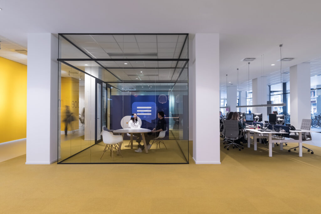 Twee mensen zitten in een glazen vergaderruimte in een modern kantoor aan de Vijzelstraat.