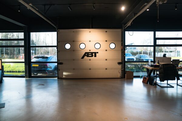 Interieur van een moderne garage aan de Frankfurtstraat met een gesloten garagedeur met ABT-logo, auto's buiten en een werkplek rechts.