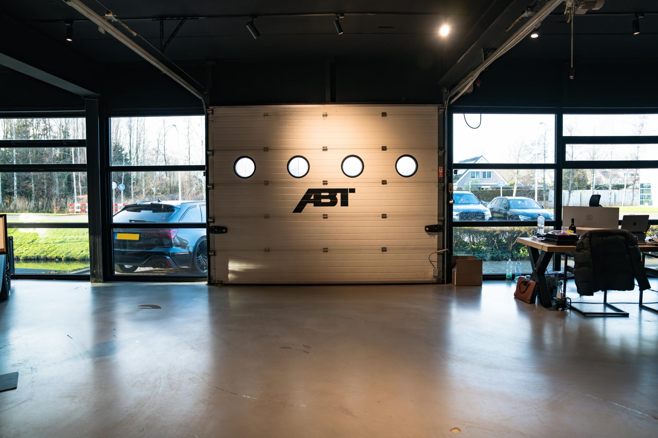 Interieur van een moderne garage aan de Frankfurtstraat met een gesloten garagedeur met ABT-logo, auto's buiten en een werkplek rechts.