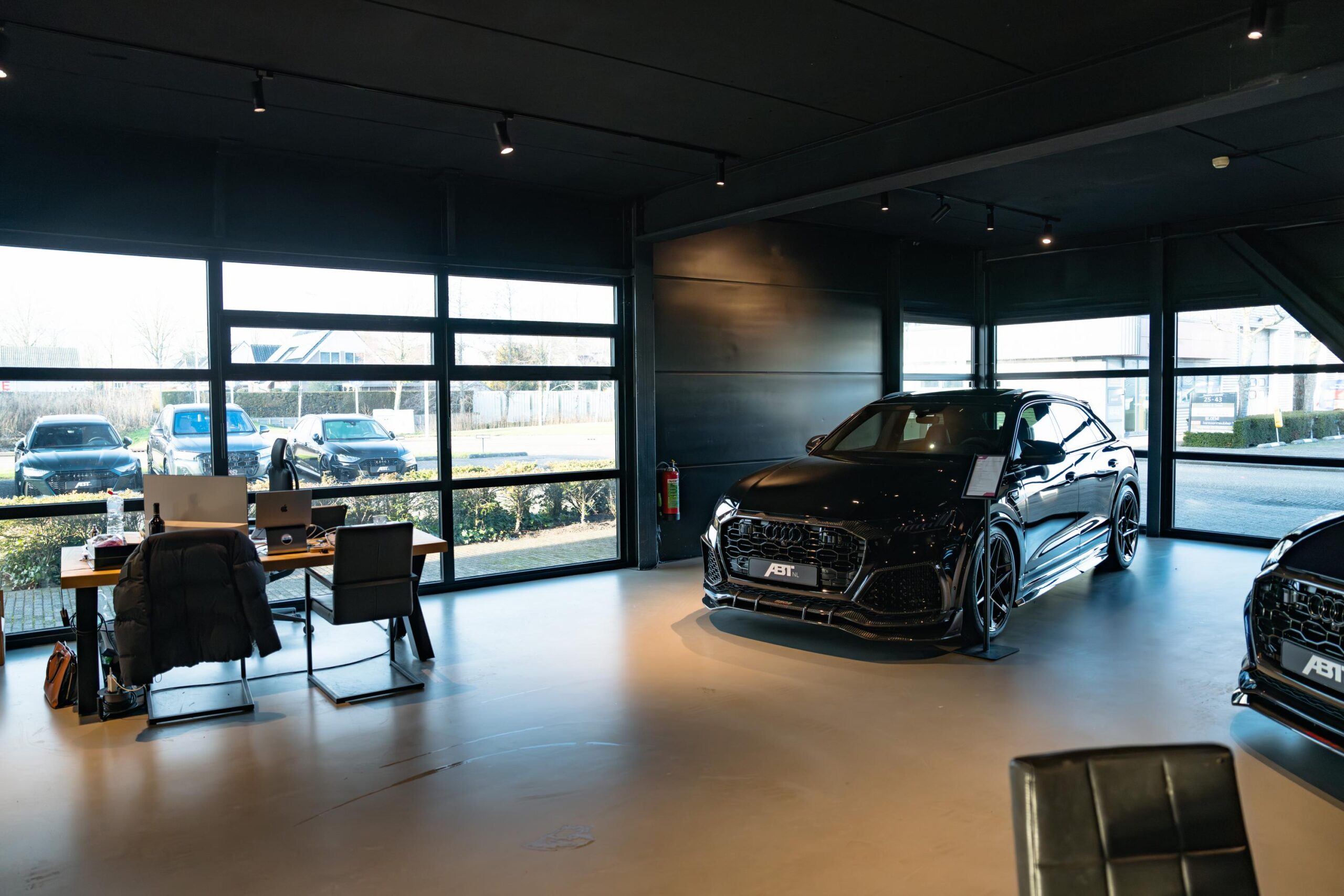 Moderne showroom aan de Frankfurtstraat met luxe zwarte Audi ABT en werkplekken bij het raam.