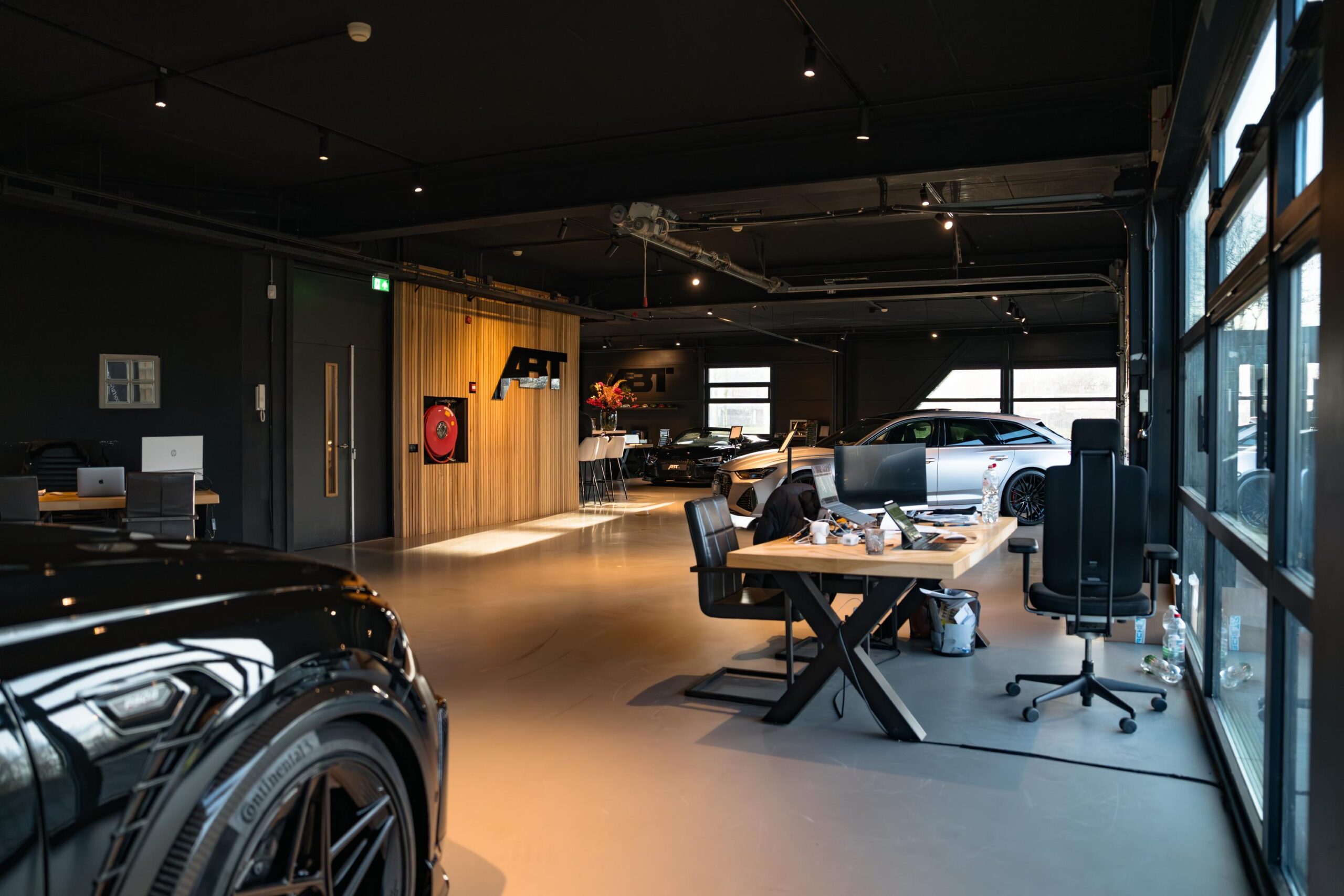 Moderne showroom en kantoorruimte van ABT Sportsline aan de Frankfurtstraat met sportauto’s en werkplekken.