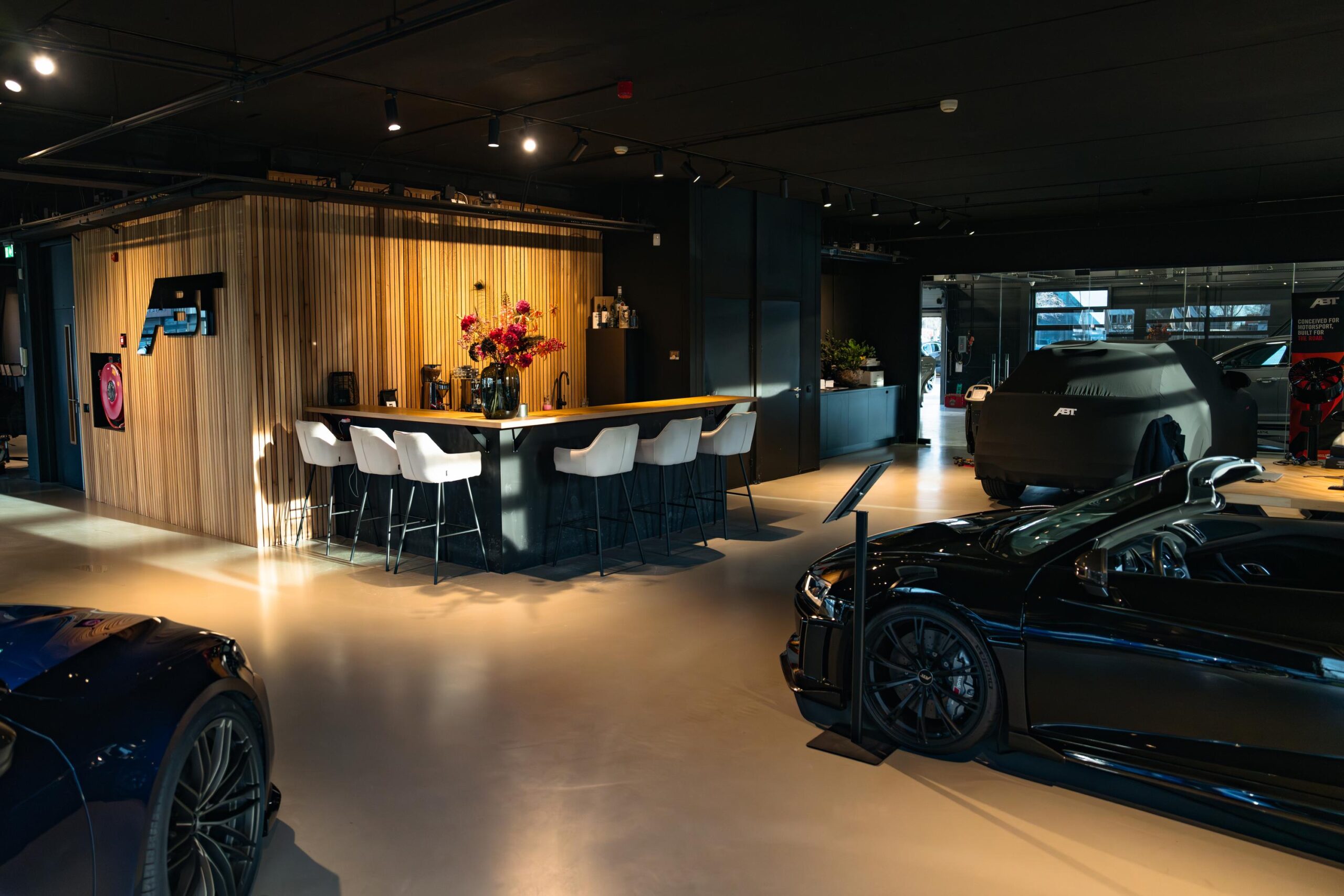 Moderne showroom aan de Frankfurtstraat met luxe sportwagens, een stijlvolle bar en ABT-branding.