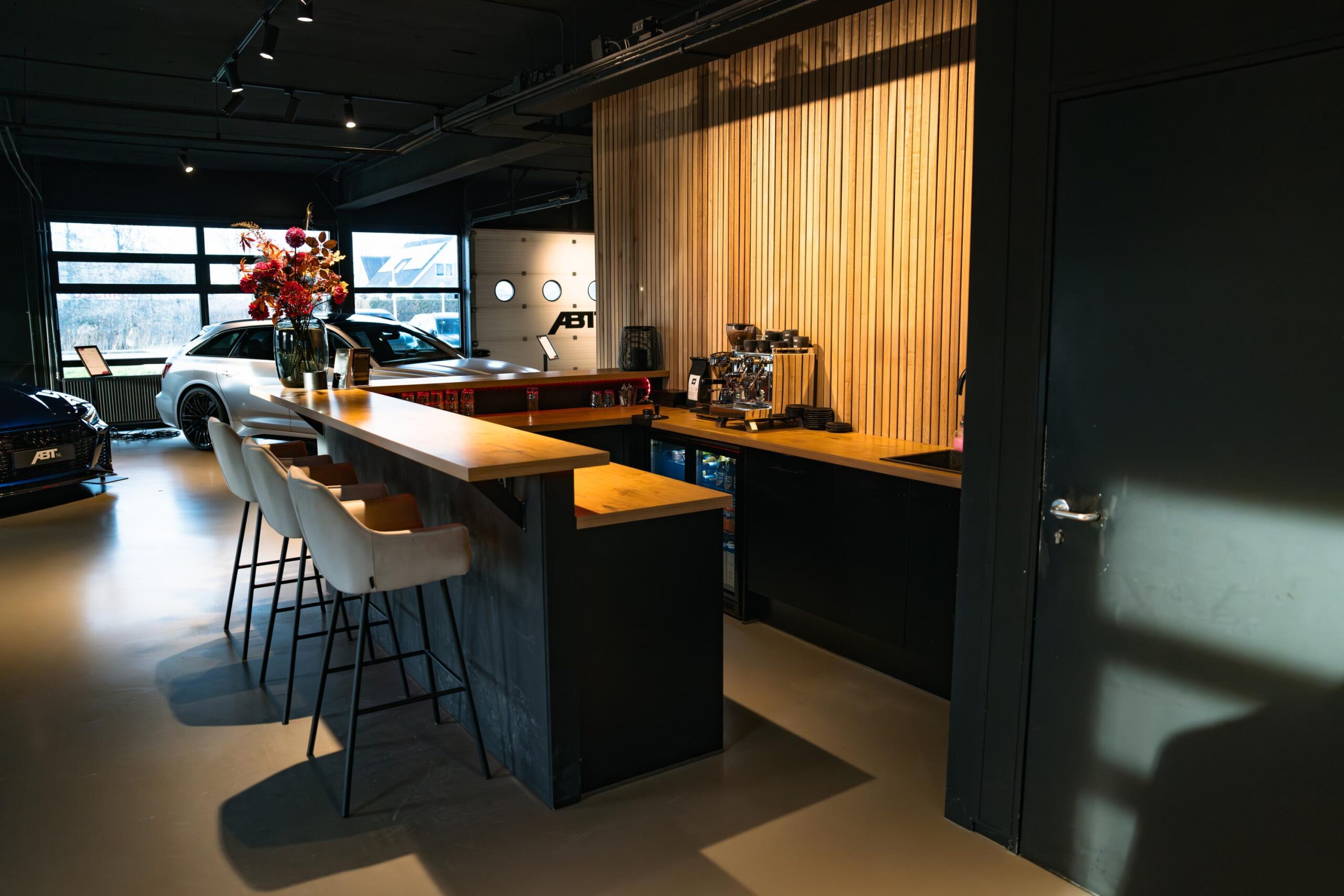 Moderne koffiebar met barkrukken in een luxe autodealer aan de Frankfurtstraat met zicht op geparkeerde ABT-auto’s.