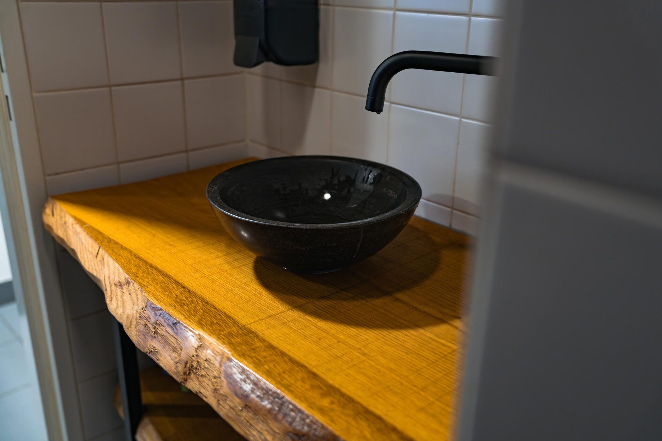 Zwarte waskom op een houten blad met boomstamrand in een betegelde hoekruimte aan de Frankfurtstraat.