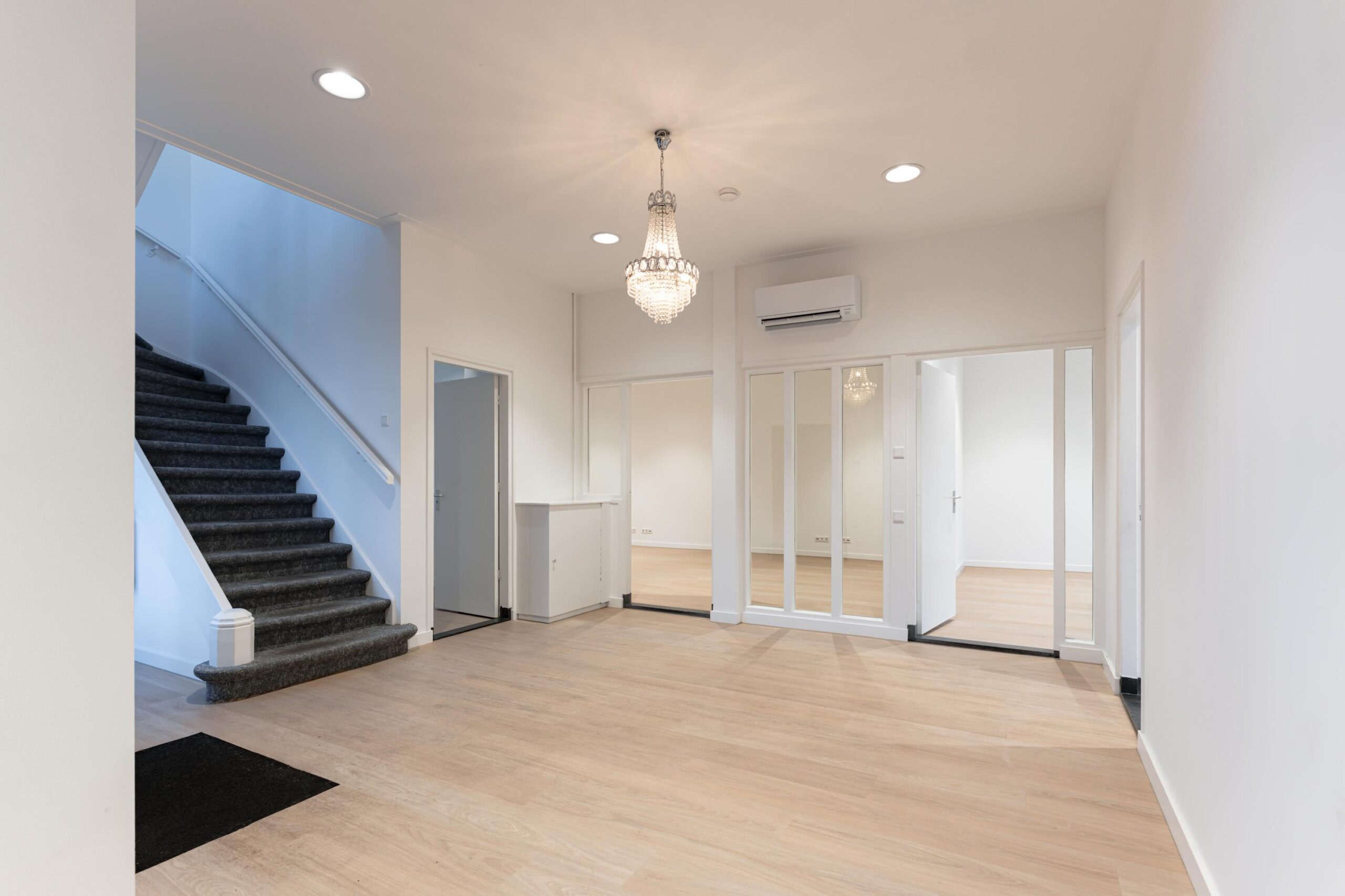 Lichte, ruime hal met houten vloer, trap, glazen deuren en een kroonluchter aan het plafond op de Biltstraat.