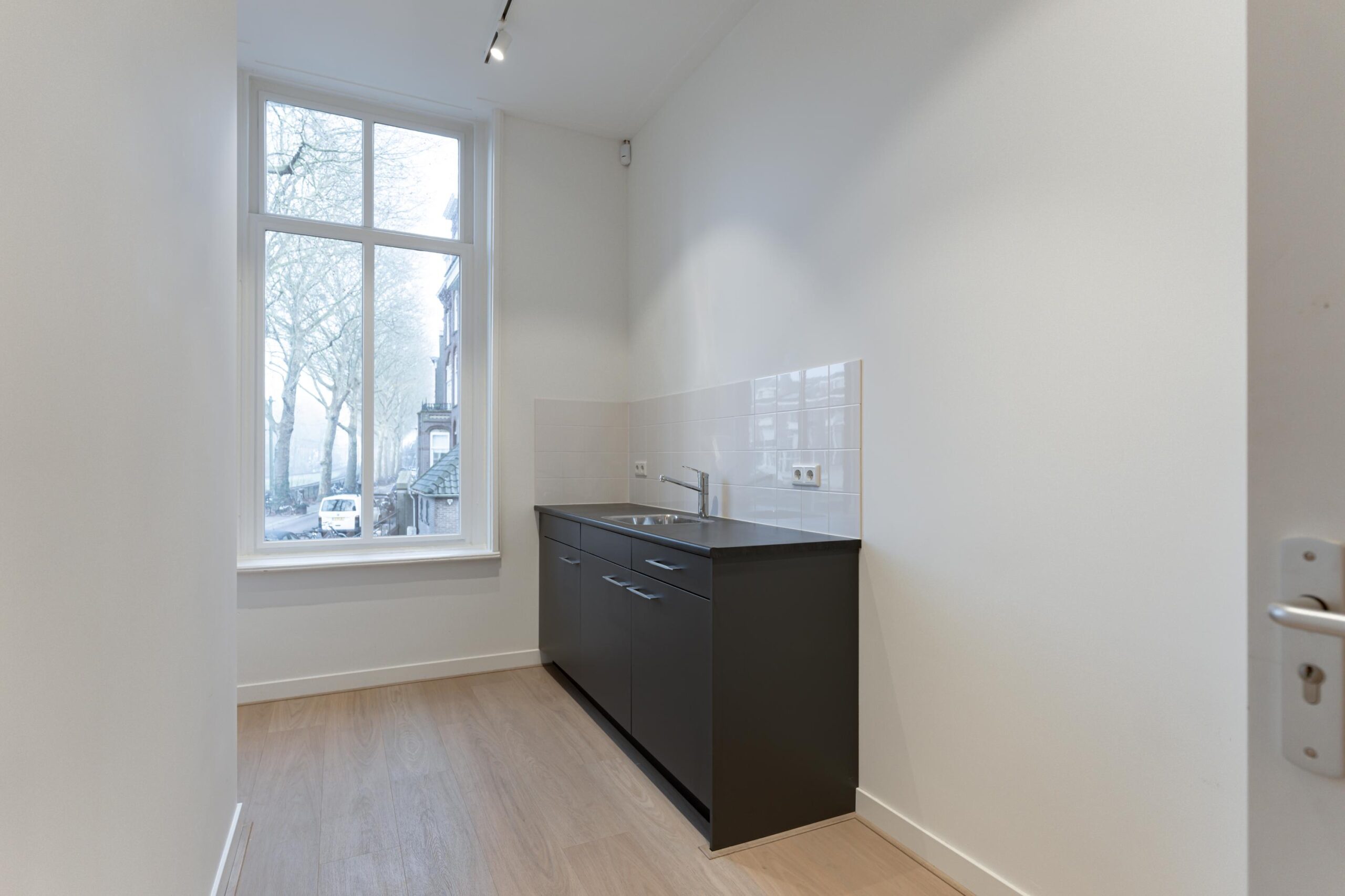 Smalle keuken met donker aanrecht, witte tegels en groot raam met uitzicht op de Biltstraat.