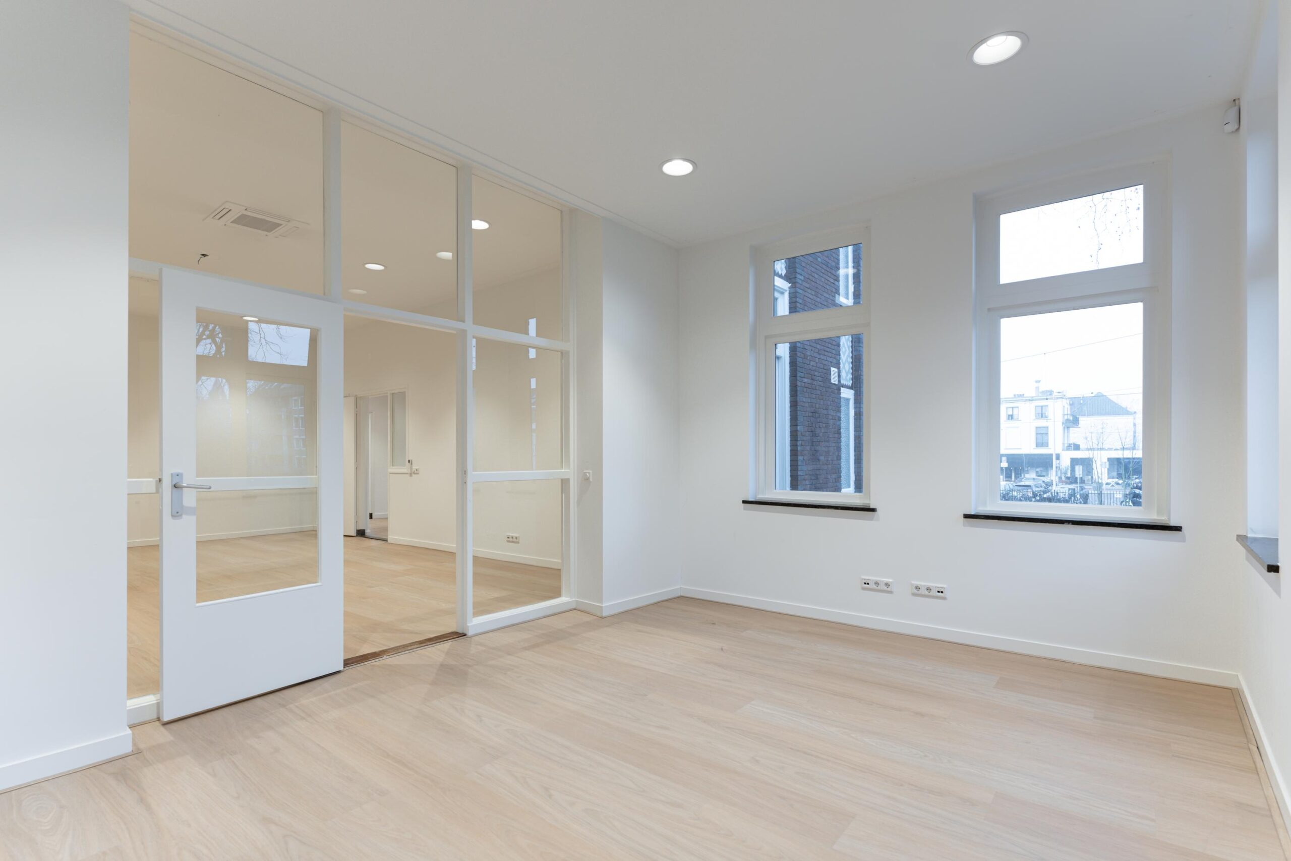 Lichte, lege kantoorruimte aan de Biltstraat met houten vloer, grote ramen en glazen tussenwand.