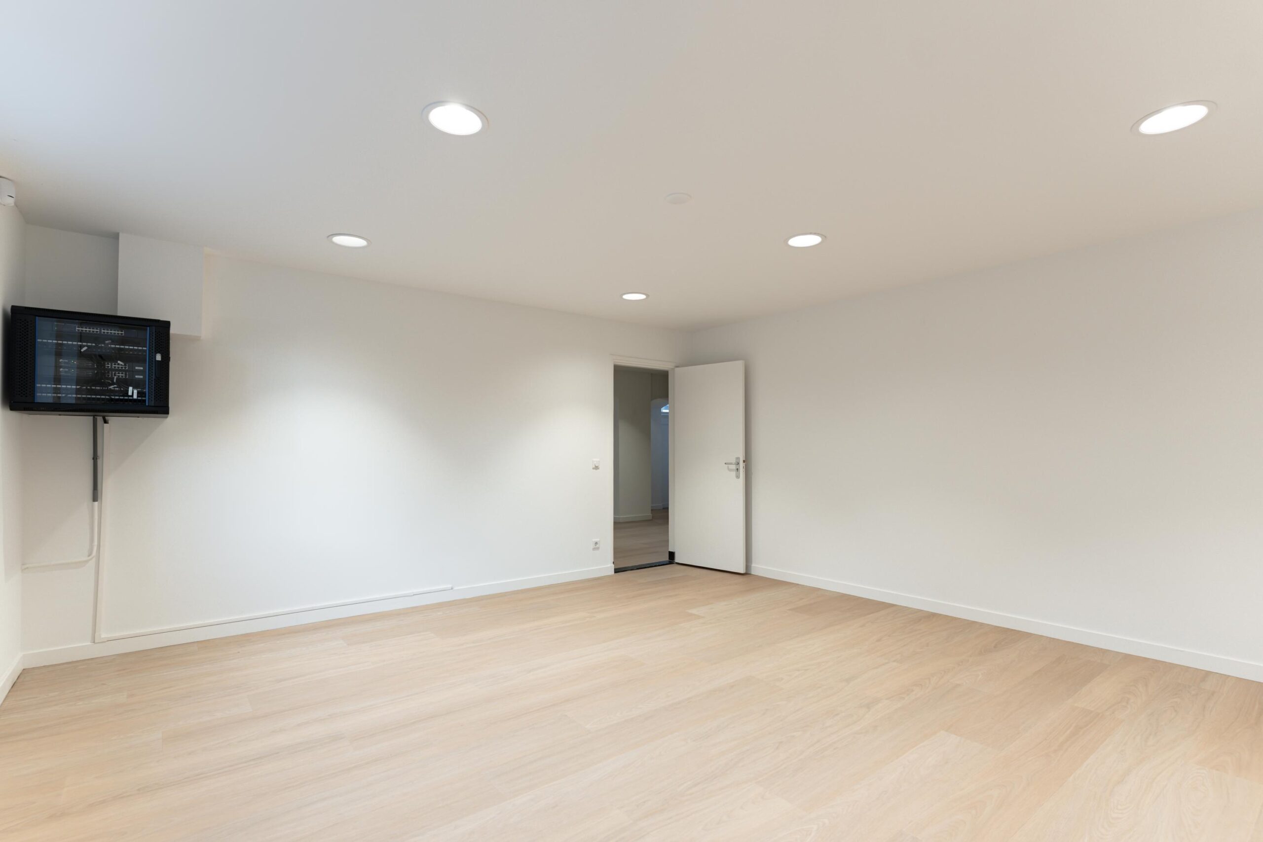 Lege kamer met houten vloer, witte muren, plafondspots en een open deur aan de Biltstraat.