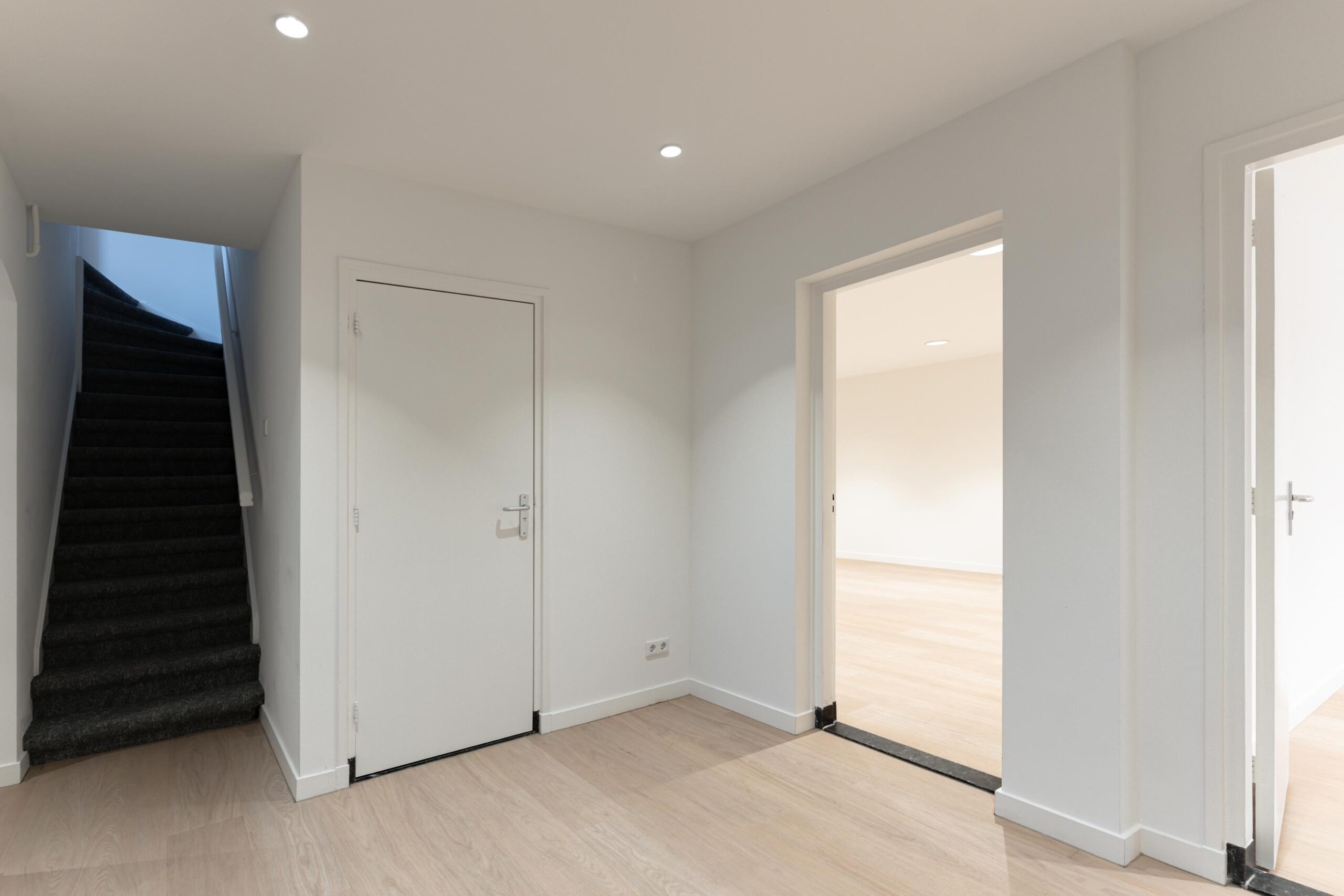 Moderne, lichte hal in een woning aan de Biltstraat met een trap, gesloten deur en twee open doorgangen naar andere kamers.