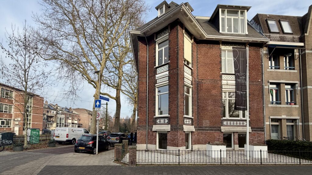 Hoekpand aan de Biltstraat in Utrecht met een groot verticaal spandoek en geparkeerde auto's langs de straat.