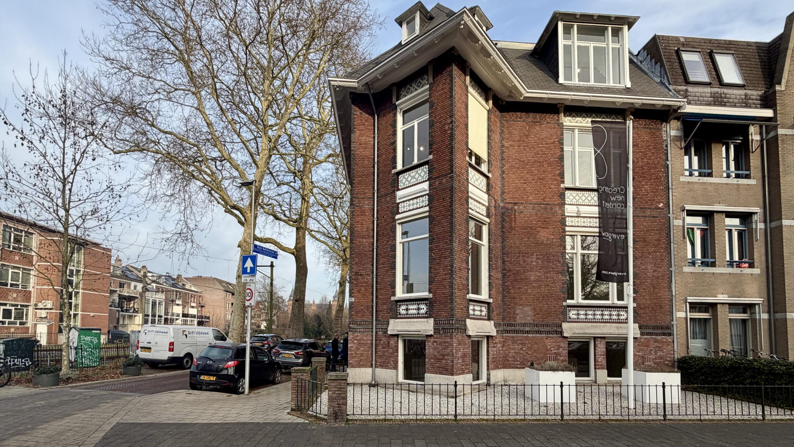 Hoekpand aan de Biltstraat in Utrecht met een groot verticaal spandoek en geparkeerde auto's langs de straat.