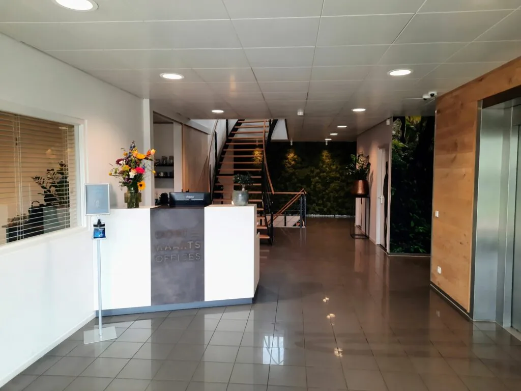 Moderne kantoorentree van Oostwaarts Offices met receptiebalie, trap en groene wanddecoratie.