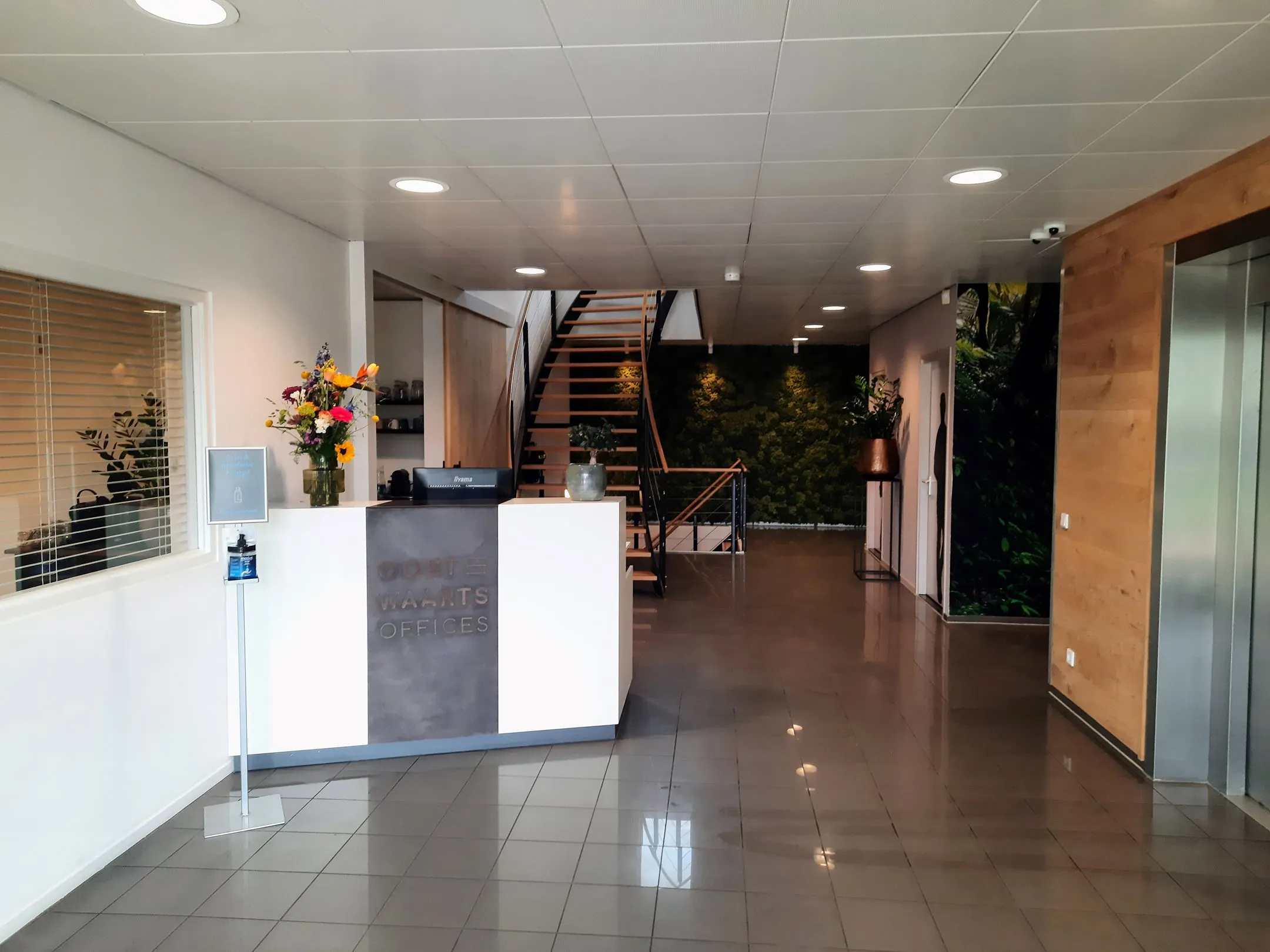 Moderne kantoorentree van Oostwaarts Offices met receptiebalie, trap en groene wanddecoratie.