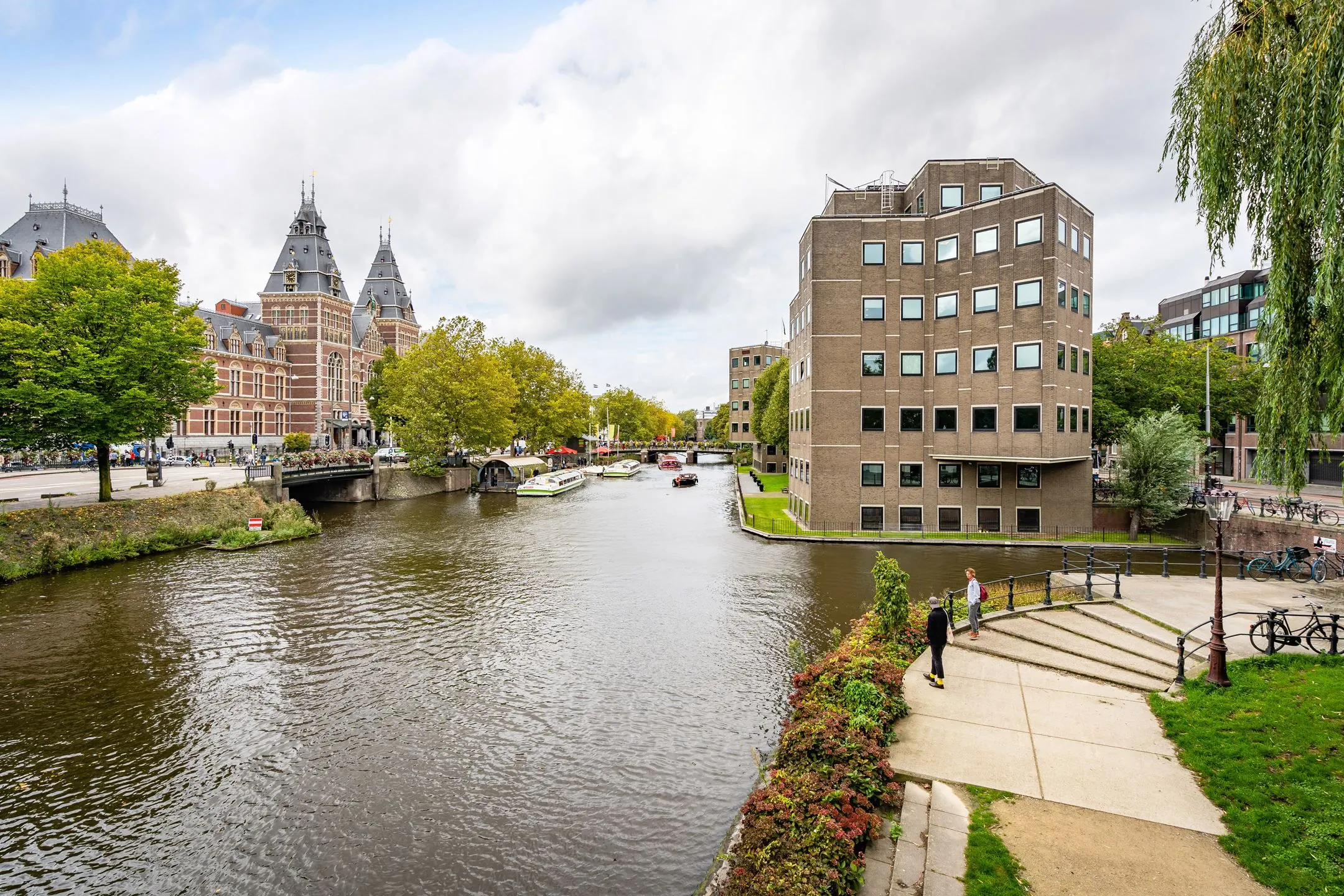 Uitzicht op de gracht bij het Rijksmuseum in Amsterdam met boten, groen en omliggende gebouwen.
