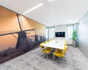Moderne vergaderruimte met geel meubilair en een grote muurfoto van de Kinderdijkse molens.