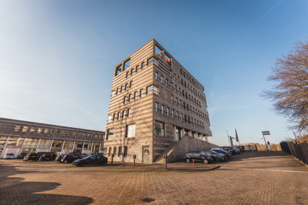Een modern kantoorgebouw met parkeerplaats op een zonnige dag.