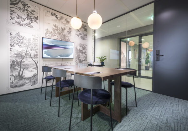 Een moderne vergaderruimte met een houten tafel, blauwe stoelen, en artistieke wanddecoratie.