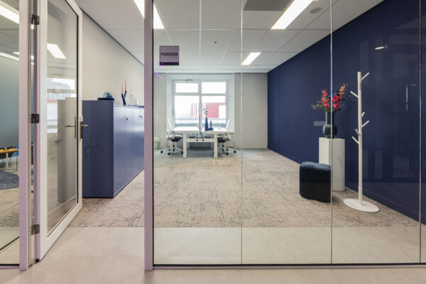 Een modern ingericht kantoor met glazen deuren, blauwe accenten en een plant in een vaas.