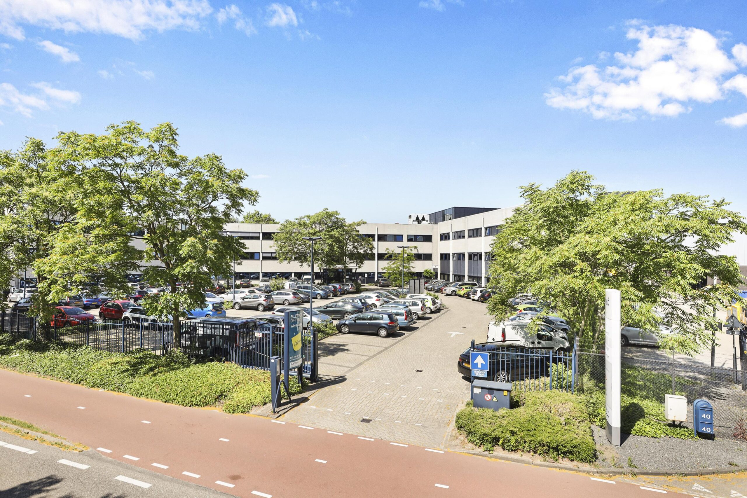 Een kantoorgebouw met parkeerterrein aan de Winthontlaan onder een heldere blauwe lucht.