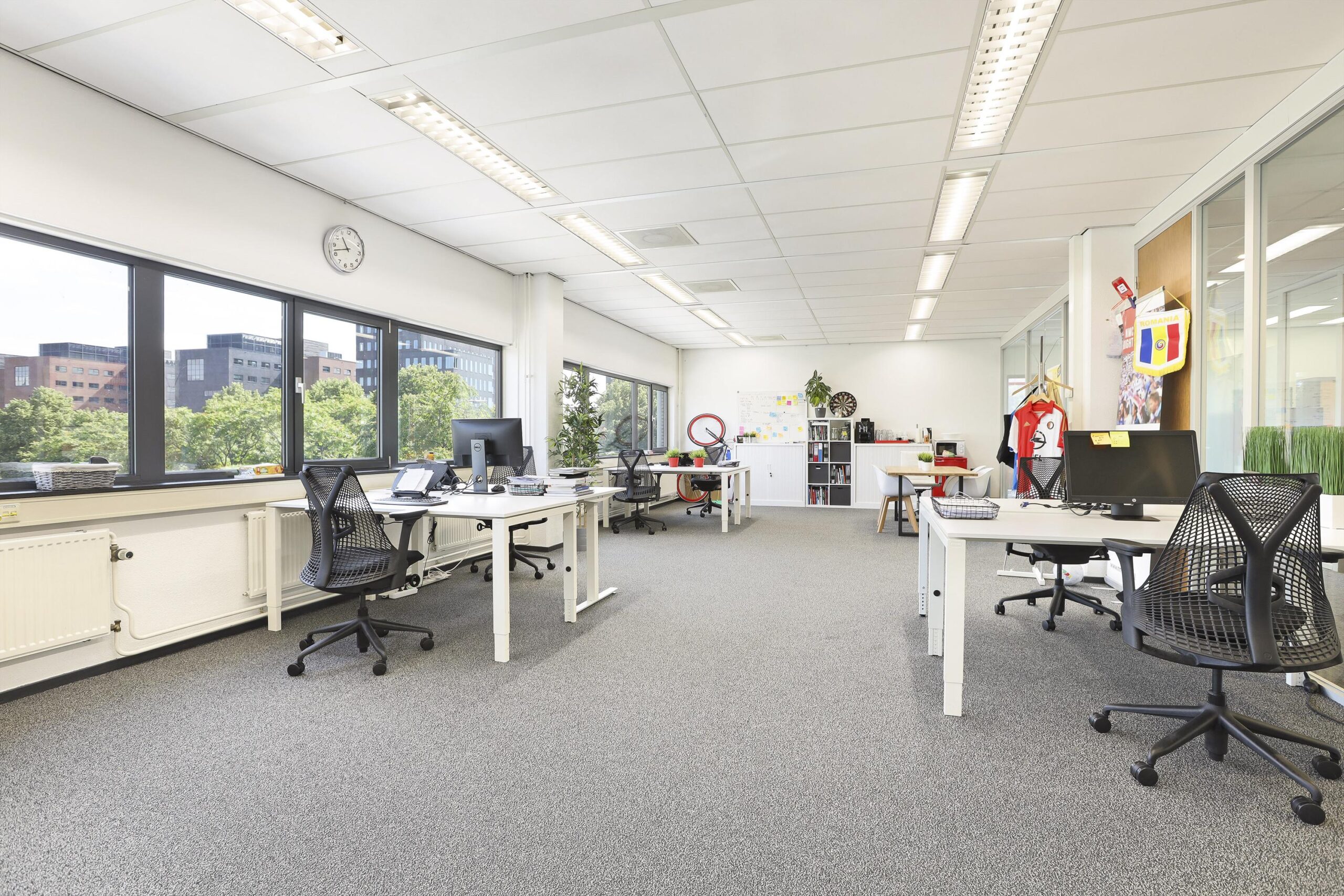 Een moderne, lichte kantoorruimte met meerdere werkplekken, grote ramen en planten.