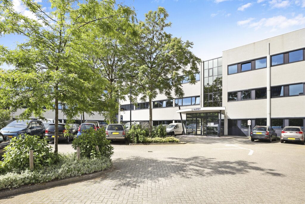 Een modern kantoorgebouw aan de Winthontlaan, omgeven door een parkeerplaats met auto's en veel groen.