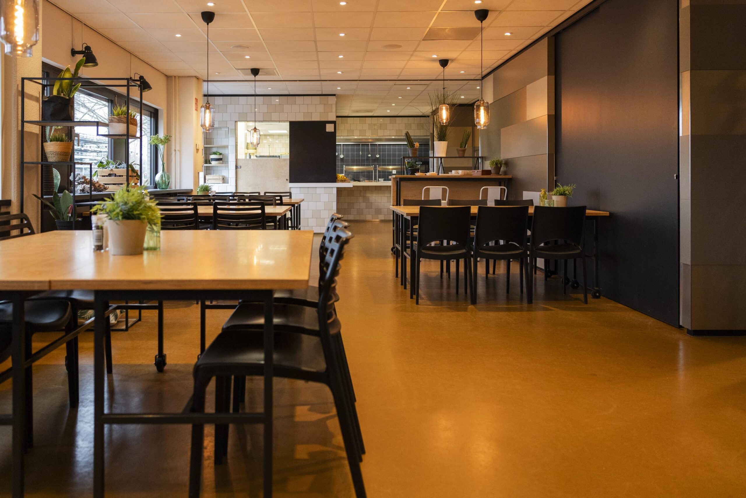 Een moderne en ruime eetruimte met houten tafels, zwarte stoelen en groene planten.
