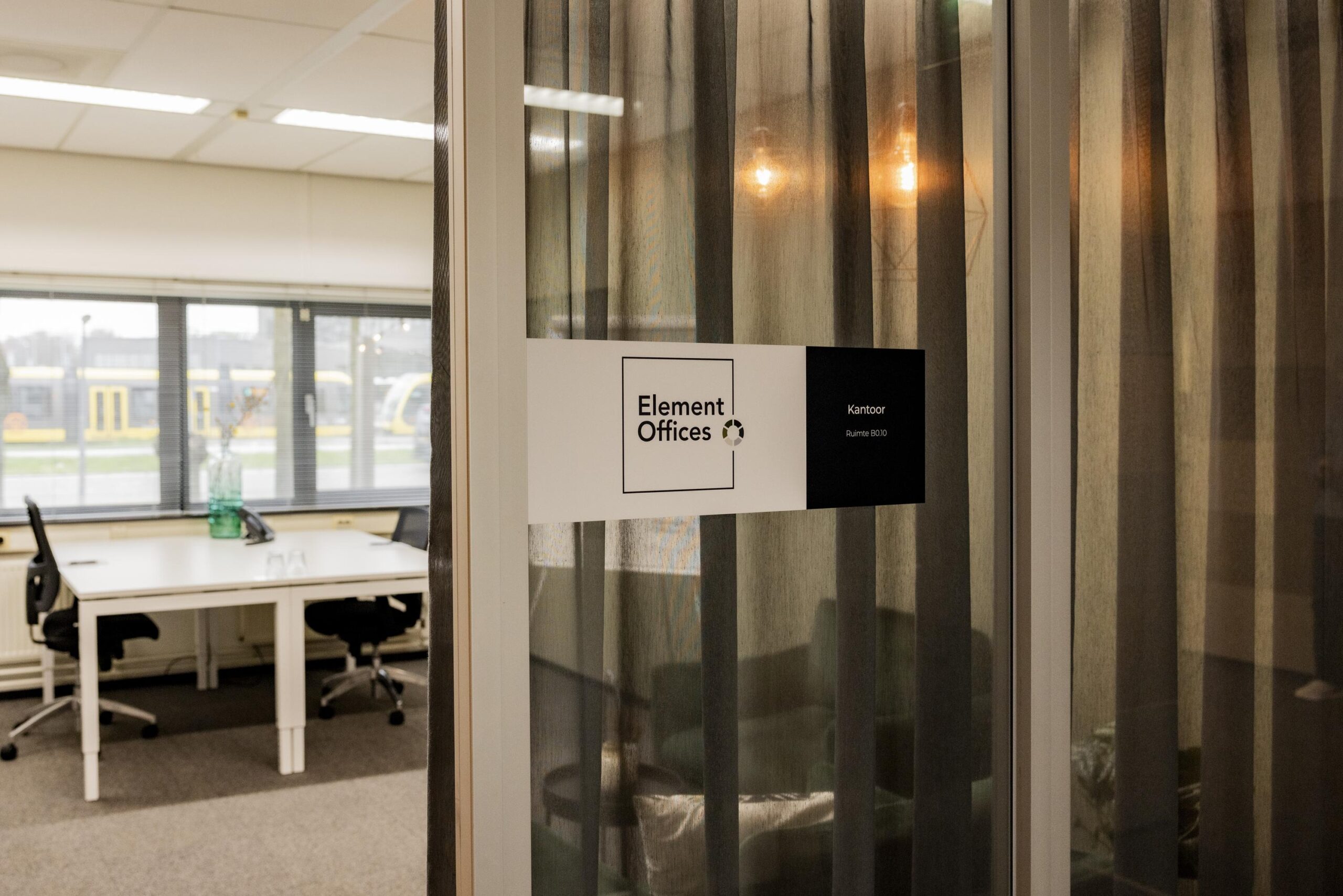 Een kantoorruimte van Element Offices met zichtbare bureaus en stoelen door een glazen wand met een naambordje.