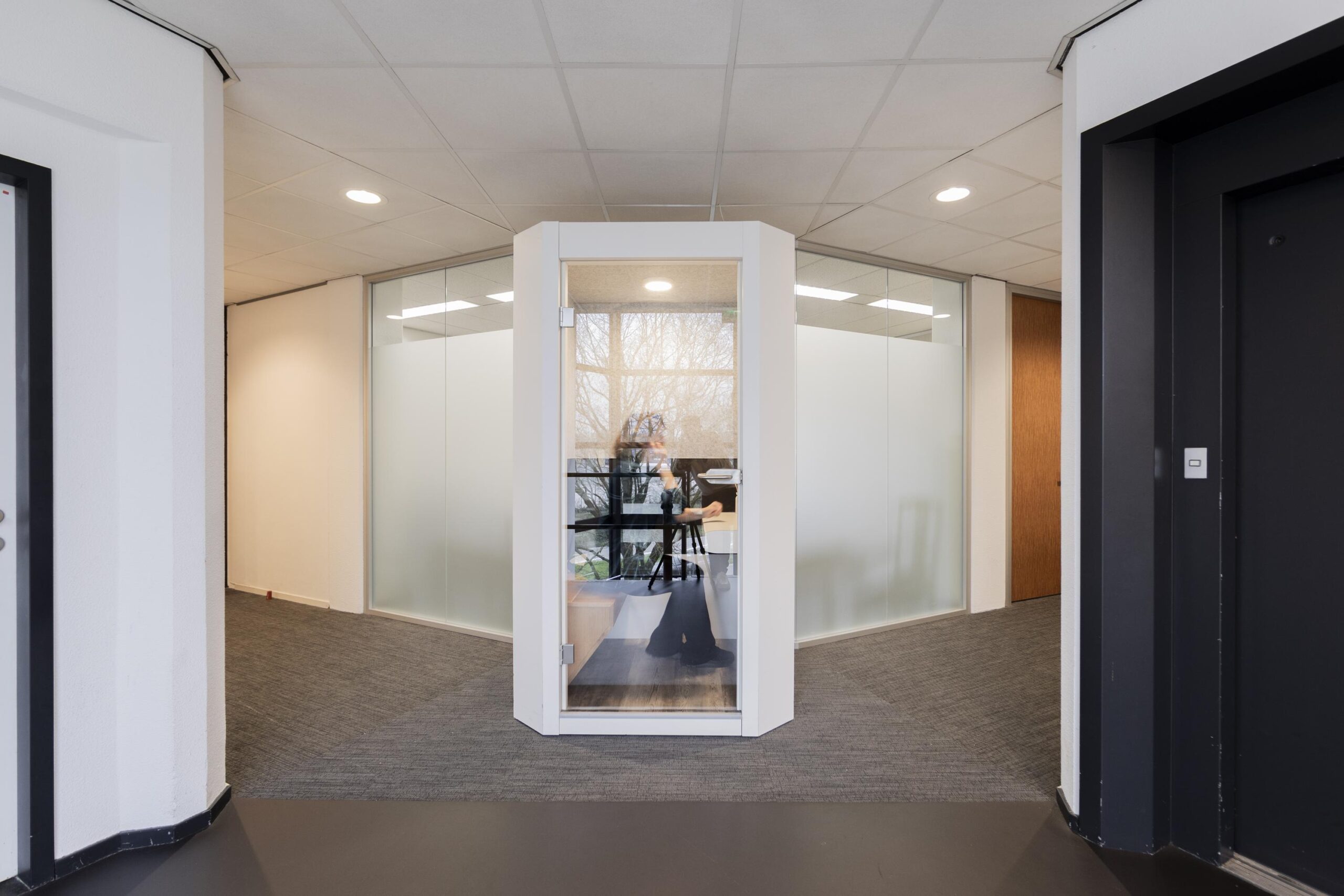 Een moderne kantoorruimte met glazen wanden en een glazen cabine in het midden.