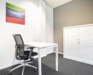 Modern en minimalistisch kantoor met een wit bureau, zwarte bureaustoel, witte opbergkast en kleurrijk abstract schilderij aan de muur.
