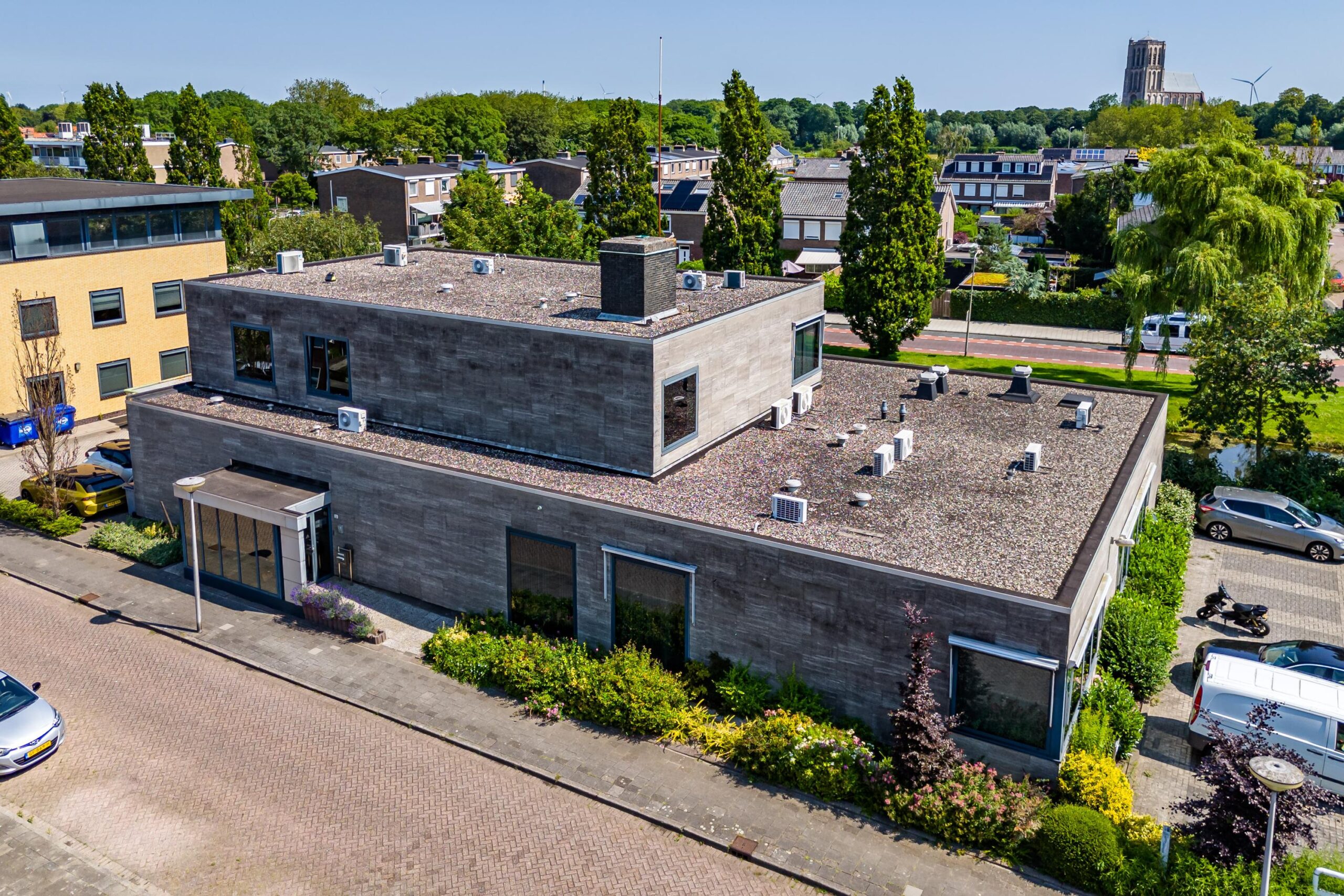 Luchtfoto van een modern, grijs gebouw aan de Nicolaas Pieckstraat, omgeven door groen met een karakteristieke toren op de achtergrond.
